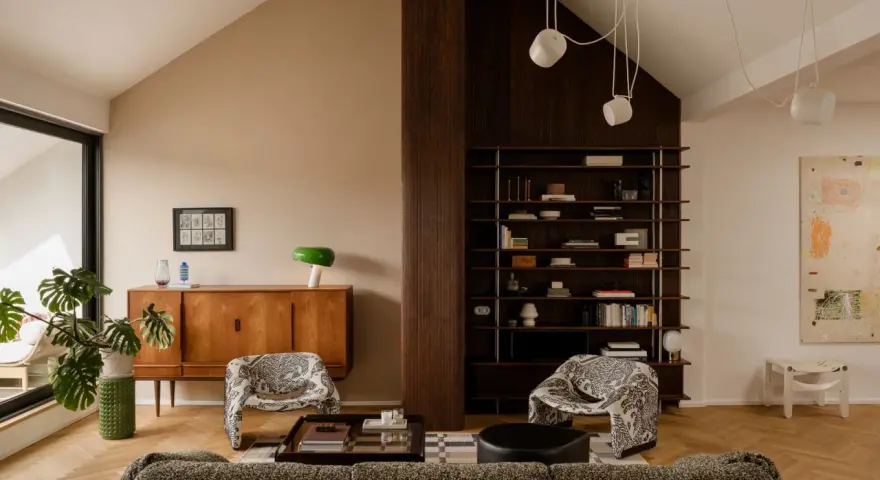 Salón acogedor con **techo inclinado interior**, muebles de madera, estanterías y sillones estampados.