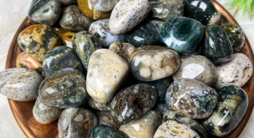 Montón de piedras jaspe blanco pulidas, con vetas verdes, marrones y amarillas. Sus propiedades son conocidas por su conexión con la naturaleza.