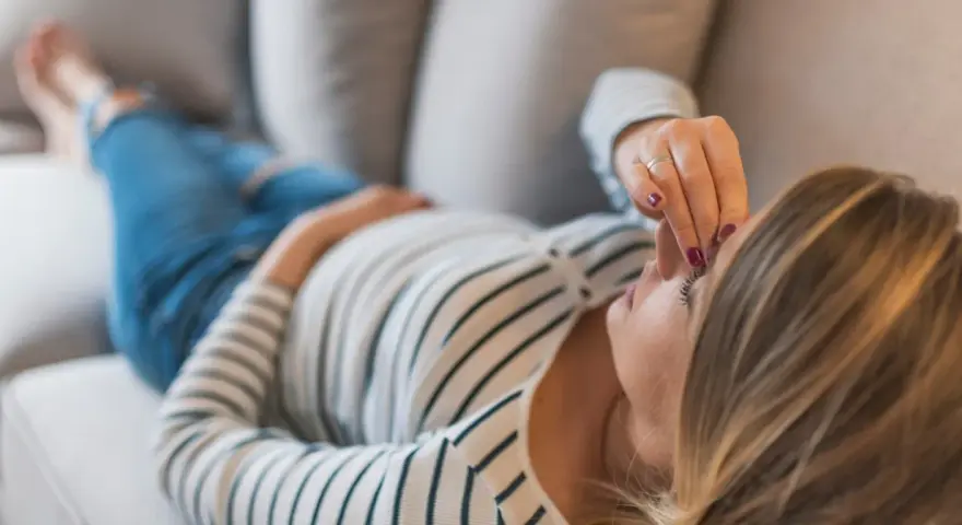 Kobieta w ciąży leży na kanapie, dotykając czoła. Zmartwienie o brak bicia serca w 8 tygodniu ciąży maluje się na jej twarzy.