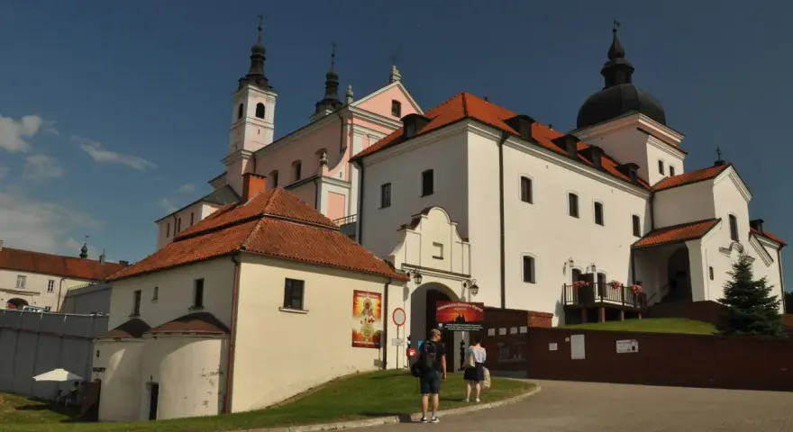 Białe budynki z czerwonymi dachami, wieże i kopuła tworzą malowniczy klasztor kamedułów.