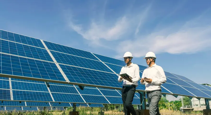 Deux hommes en casque blanc inspectent un champ de panneaux solaires, discutant d'un bail emphytéotique photovoltaïque sous un ciel bleu.
