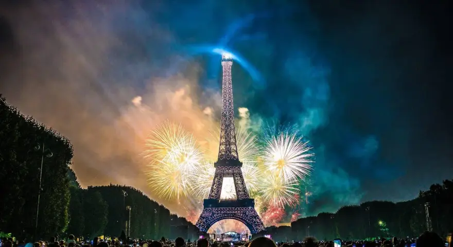 Espectacular espectáculo de fuegos artificiales ilumina la Torre Eiffel, celebrando porque se celebra el 14 de julio en Francia. Multitud observa.
