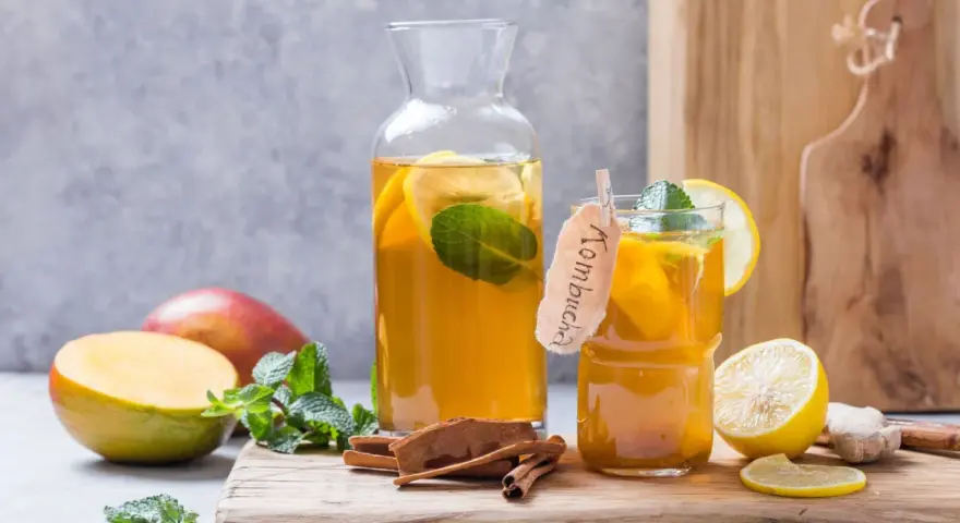 Verre et carafe de kombucha thé rafraîchissant avec des tranches de citron, de la menthe, des bâtons de cannelle et des mangues.
