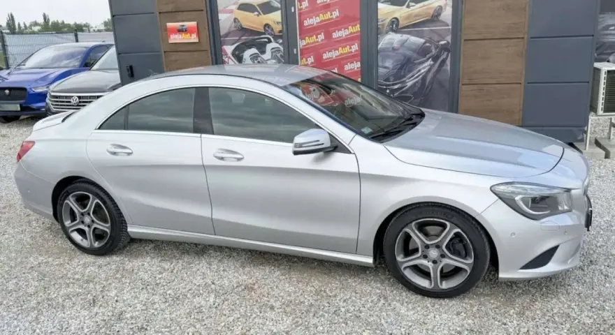 Srebrny Mercedes CLA na tle salonu samochodowego z reklamami.