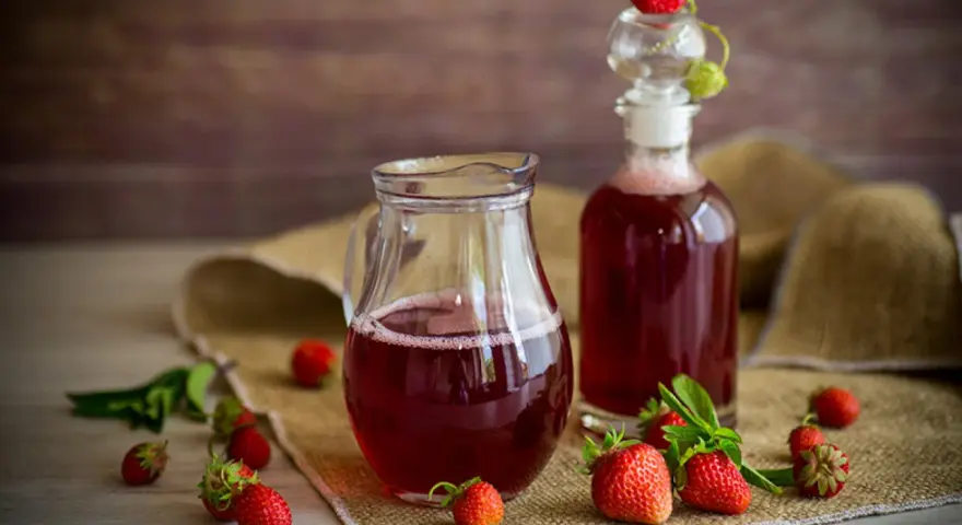 Frischer Erdbeersirup in Karaffe und Flasche, umgeben von reifen Erdbeeren. Perfekt, um Erdbeersirup selber machen.