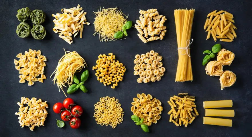 Różnorodne włoskie dania z makaronem: od tagliatelle i spaghetti po farfalle i penne, z dodatkiem pomidorków i bazylii.