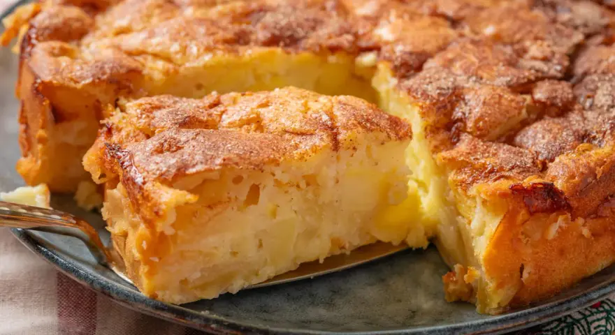 Ein saftiger apfelkuchen mit schale, goldbraun gebacken und mit Zimt bestreut. Ein Stück wird gerade herausgehoben.
