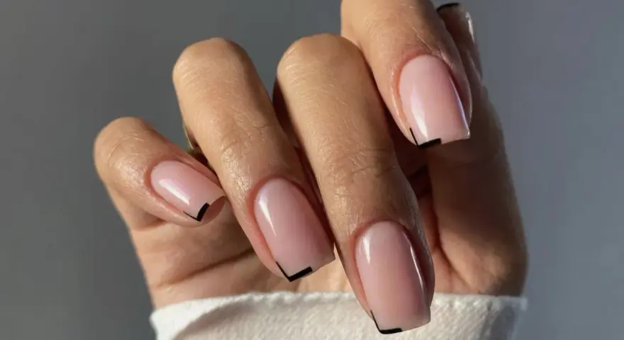 Mano con unghie quadrate naturali, smalto rosa tenue e un sottile dettaglio grafico nero sulla punta.