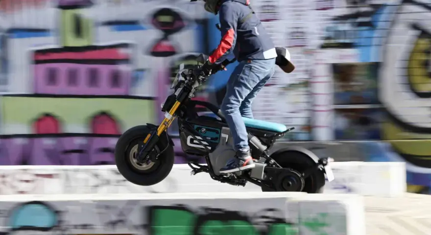 Młody mężczyzna na elektrycznym motocyklu BMW CE02 wykonuje skok na tle kolorowego graffiti.