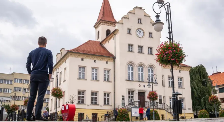 Mężczyzna podziwia ratusz, jedną z głównych trzebnickich atrakcji. W tle kwitnące pelargonie i zabytkowa architektura.