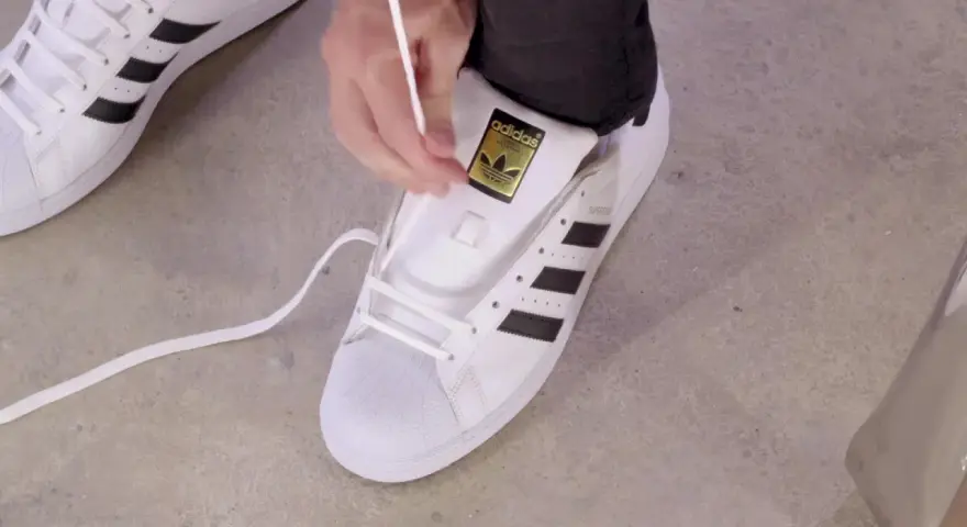Pokazuję, jak wiązać sznurówki w adidasach Superstar. Białe sznurówki przeplatane przez czarne paski.