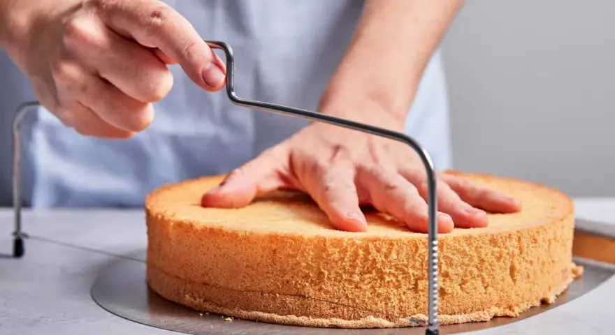 Hände schneiden mit einem Tortenbodenschneider einen Biskuitboden für ein einfaches Cassata Rezept.