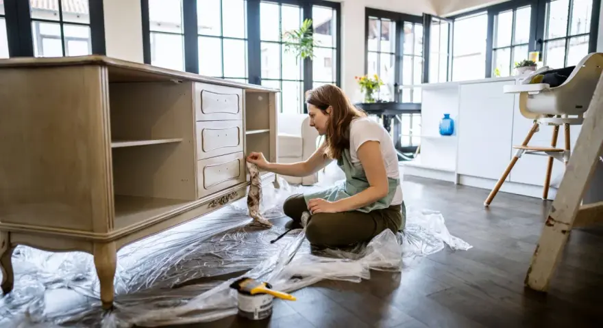 Mujer lijando muebles de madera antiguos para restaurarlos.