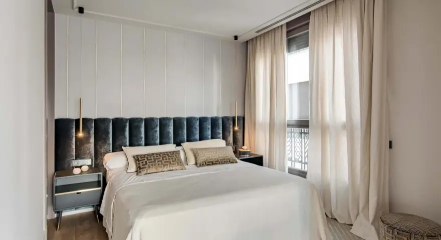 Acogedora habitación pequeña con cama grande, cabecero tapizado, mesitas de noche modernas y cortinas elegantes.