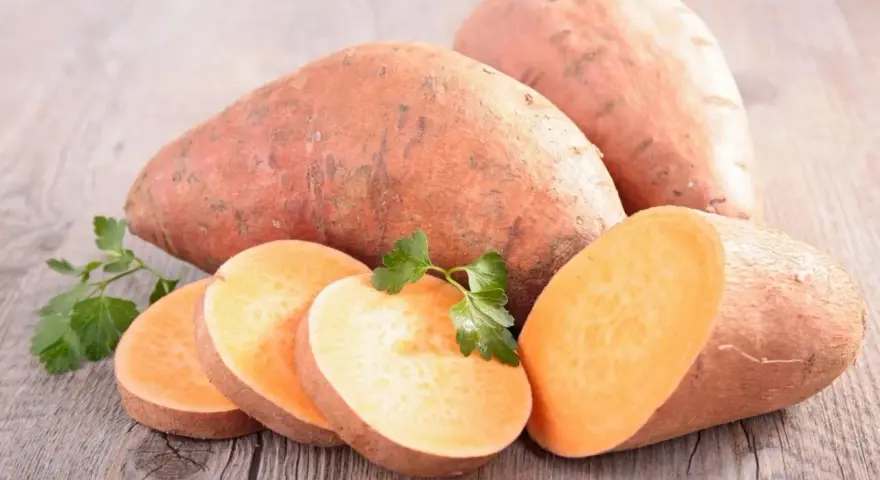 Patates douces entières et tranchées, prêtes à cuire. Une touche de persil frais pour la décoration.