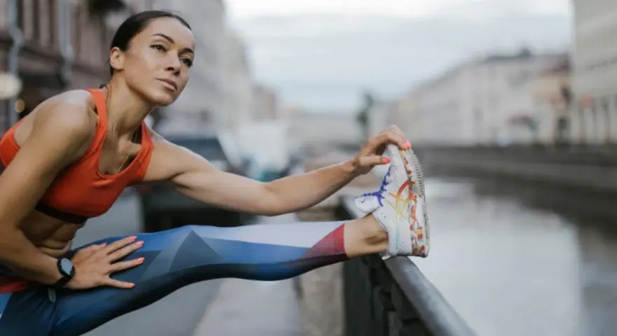Kobieta w sportowym stroju rozciąga nogę, przygotowując się do treningu cardio nad kanałem.