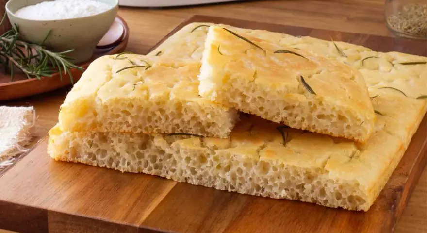 Focaccia senza glutine soffice e dorata, guarnita con rosmarino fresco, pronta per essere gustata.