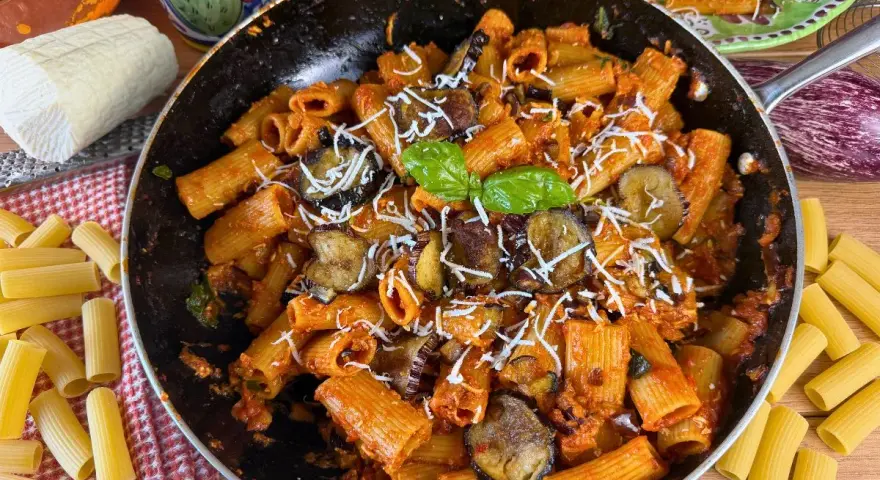 Rigatoni ricchi di melanzane fritte e pomodoro, conditi con ricotta salata grattugiata e basilico fresco. Un piatto di pasta alla norma invitante.