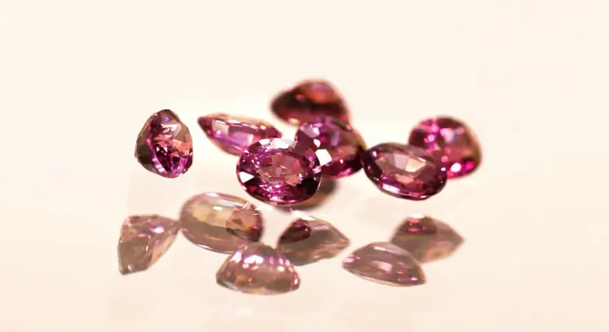 Un gruppo di pietre di granato rosa sfaccettate, che riflettono la luce su una superficie lucida.