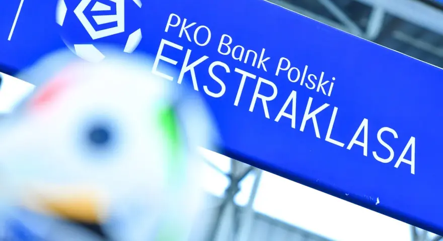 Niebieska tablica z logo PKO Bank Polski i napisem EKSTRAKLASA. W tle piłka nożna, gdy terminarz ekstraklasy.