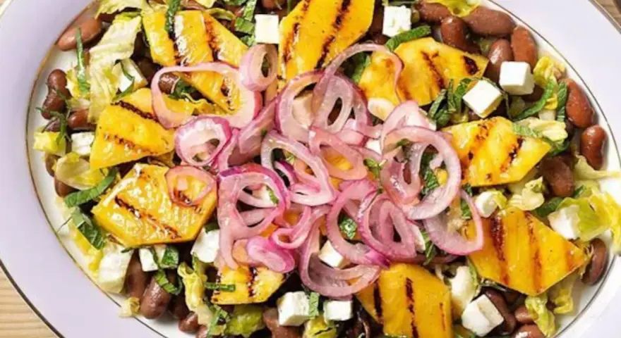 Ensalada de frijoles, piña a la parrilla, queso y cebolla morada en un plato blanco.