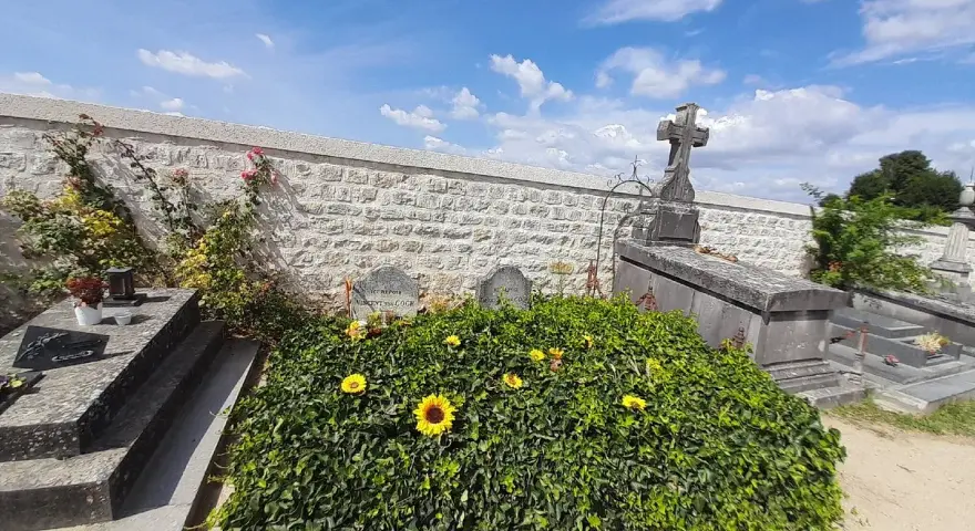La tombe de Van Gogh, recouverte de verdure et ornée de tournesols, sous un ciel bleu.
