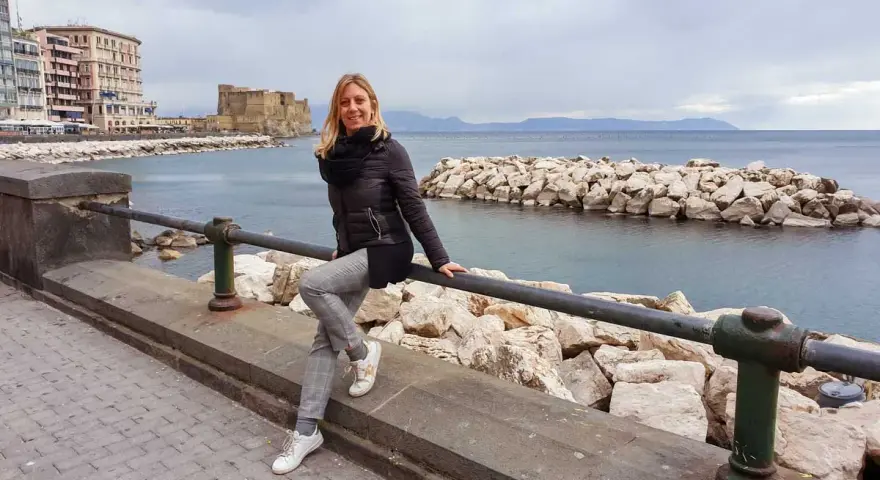 Woman sitting on a railing with Castel dell'Ovo and the sea in the background in Naples.