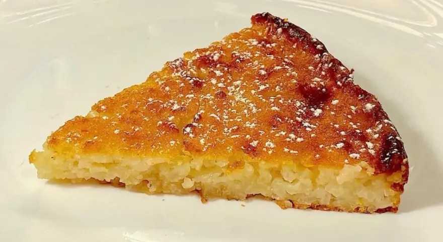 Una fetta di torta di riso, profumata e dorata, come la torta di riso ricetta della nonna, spolverata di zucchero a velo.