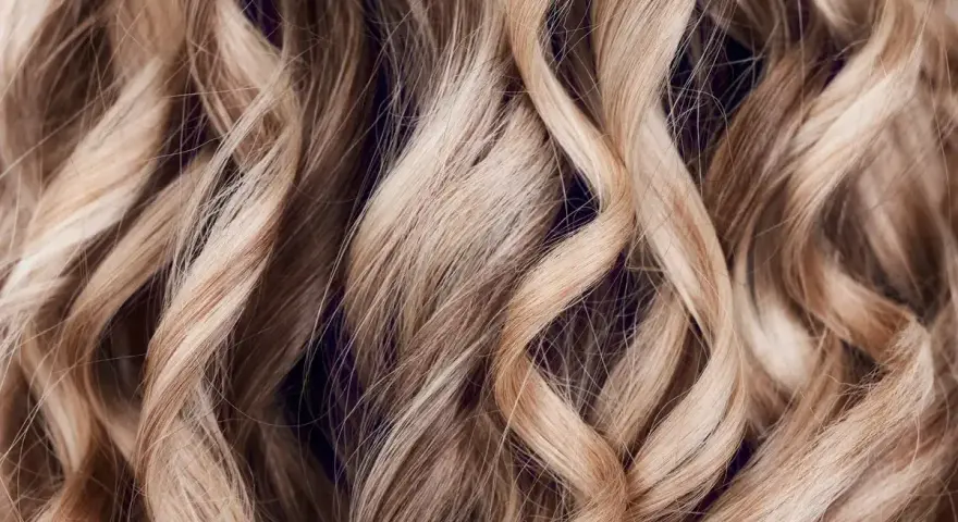 Falujące, blond włosy z subtelnymi refleksami, które mienią się w świetle, tworząc efekt głębi.