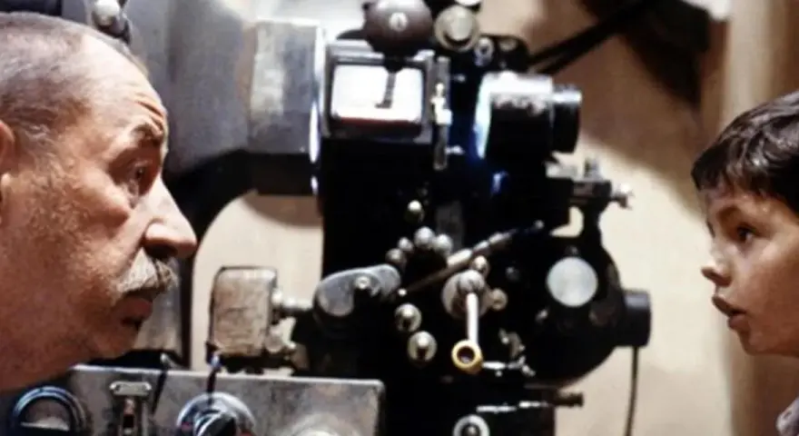 Un uomo e un bambino osservano affascinati una vecchia cinepresa, un'immagine che evoca le magiche tecniche cinematografiche.