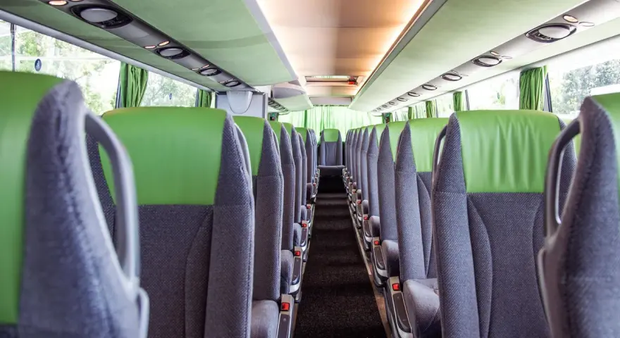 Puste siedzenia w autokarze, gotowe na podróż z Oławy do Wrocławia. Zielono-szare wnętrze, czyste i przestronne.