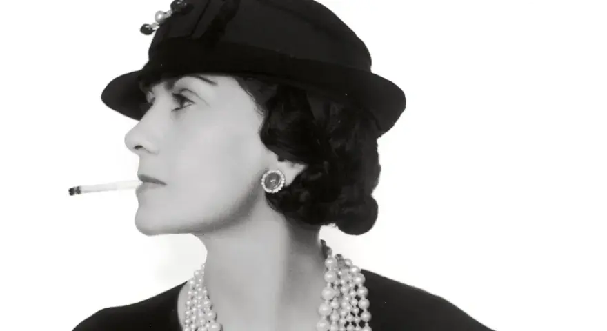 Coco Chanel, con sigaretta e perle, icona di stile, ci ricorda dove è nata Coco Chanel, un'ispirazione senza tempo.