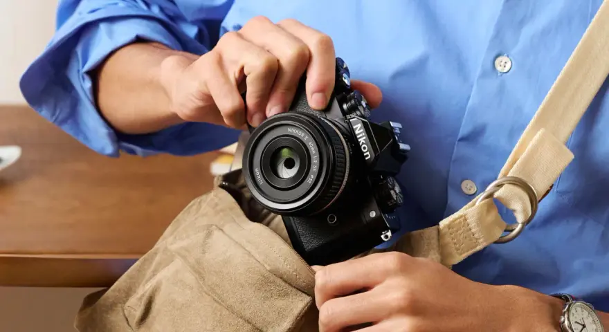 Osoba w niebieskiej koszuli wkłada czarny aparat Nikon z obiektywem do torby.