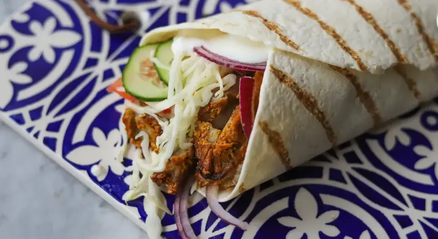 Pyszny kebab w picie z soczystym mięsem, chrupiącą kapustą, pomidorem, ogórkiem i czerwoną cebulą, podany na ozdobnym talerzu.