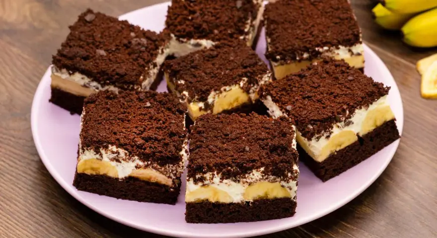 Saftiger Maulwurfkuchen vom Blech mit Bananen und Schokostreuseln auf einem rosa Teller.