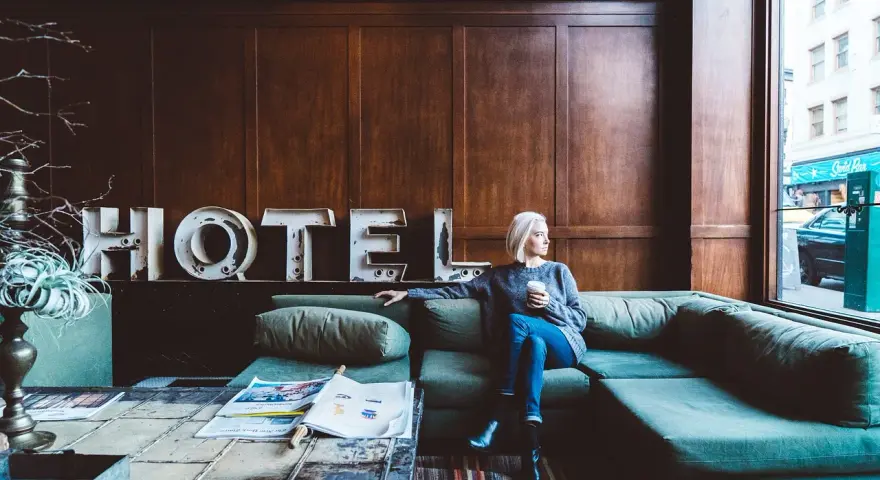 Kobieta z kawą siedzi na kanapie w hotelu. Zastanawia się, ile zarabia technik hotelarstwa.