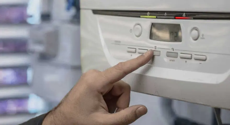 Mano presionando un botón en la caldera de gas, indicando posibles problemas. La pantalla muestra "02".