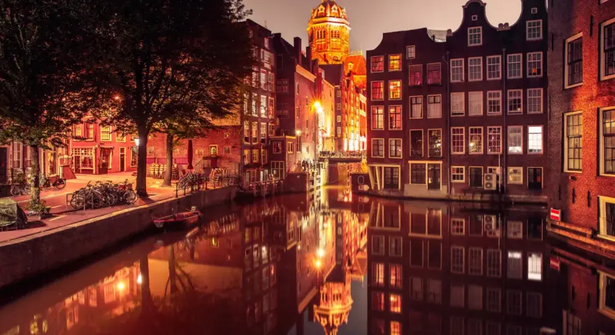 Nocny Amsterdam, kanał odbija oświetlone kamienice i kopułę kościoła. Czerwona ulica Amsterdam w blasku latarni.
