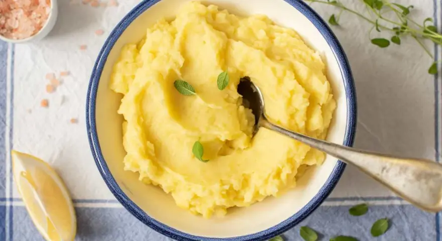 Un cremoso puré de patata de la abuela, servido en un cuenco azul, con una cuchara, limón y sal rosa.