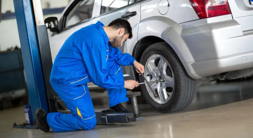 Meccanico in tuta blu lavora sulla ruota anteriore di un'auto argentata sollevata da un ponte.
