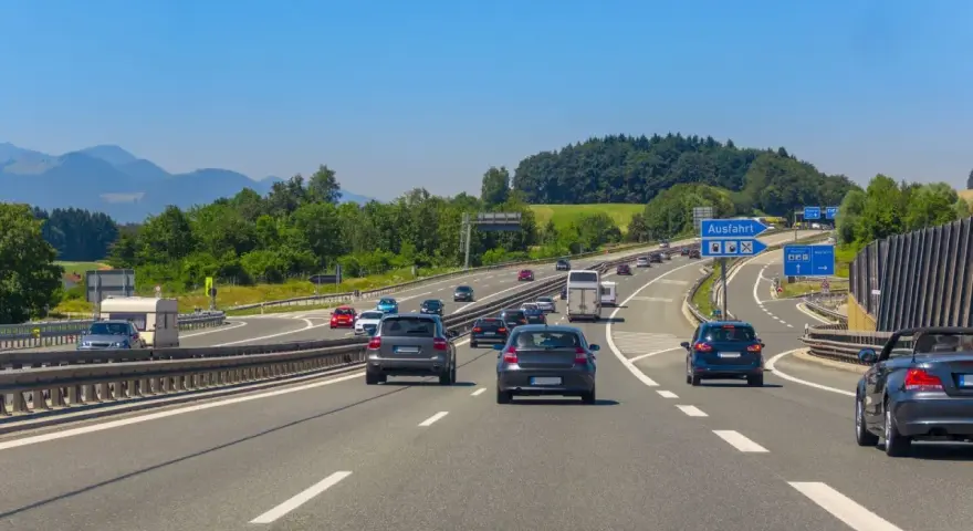 Trafik på en tysk motorväg med berg i bakgrunden. En skylt visar "Ausfahrt" (avfart), vilket indikerar en autohof i Tyskland.