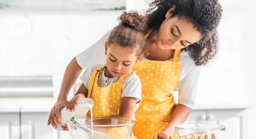 Une mère et sa fille préparent une recette, la petite verse du lait ribot dans un bol.