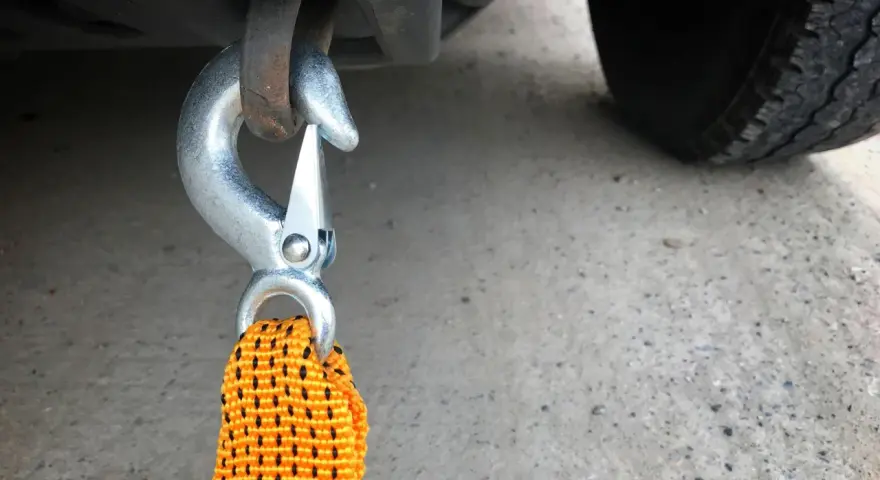 Gancio metallico agganciato al telaio di un'auto, pronto per iniziare a come trainare una macchina. La cinghia arancione è visibile.