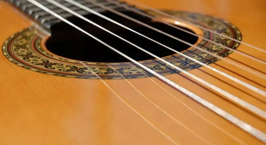 Zbliżenie na gitarę klasyczną. Sześć białych strun biegnie nad ozdobną rozetą.