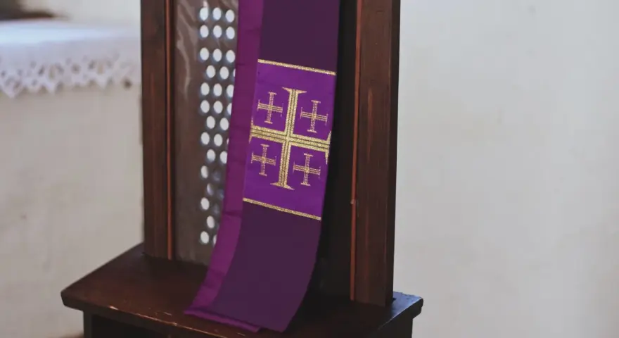 Fioletowa stuła z krzyżami, symbol przygotowania do spowiedzi wielkanocnej, wisi na drewnianej kratce konfesjonału.