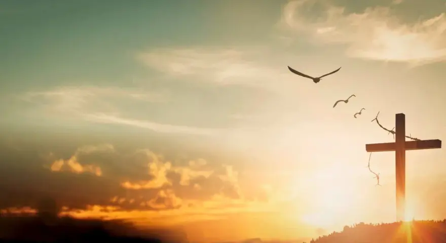 A cross on a hill, adorned with thorns, stands against a sunset sky. Birds fly overhead, symbolizing the feast of the exaltation of the holy cross.