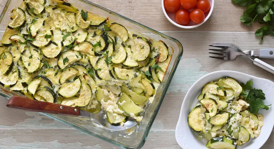 Delicioso calabacín al horno, gratinado y espolvoreado con perejil fresco. Servido en una fuente de vidrio y un plato blanco.