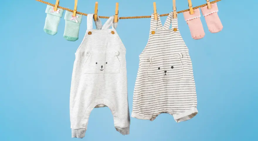 Ropa de bebé colgada para secar: dos peleles con caritas de oso y calcetines a juego. ¡El momento perfecto para saber cuando lavar la ropa del bebé!