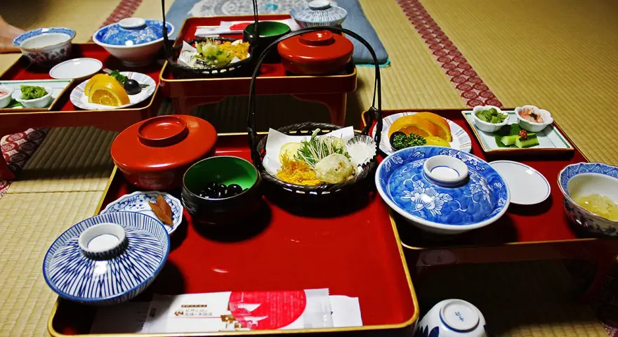 A traditional Japanese meal, perhaps a monk diet, featuring small dishes of tempura, fruit, pickles, and black beans on red lacquer trays.
