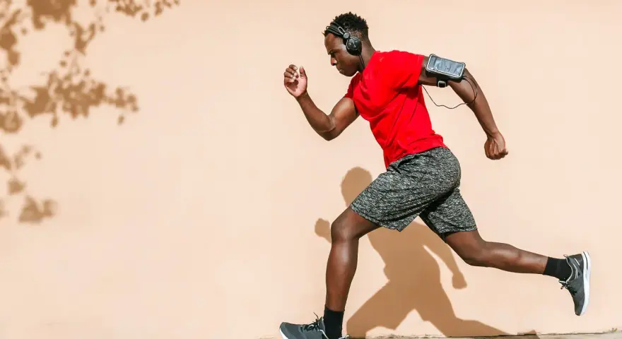 Hombre corre con audífonos y brazalete para celular. ¡Correr quema grasa y te da energía!